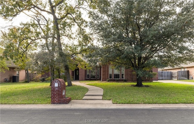 view of property hidden behind natural elements featuring brick siding, fence, and a front lawn