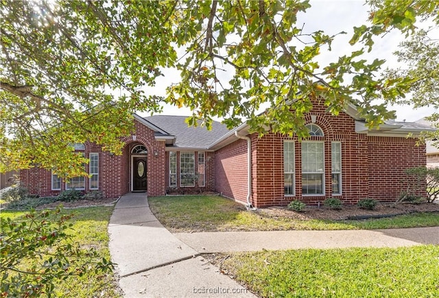 view of front of property with brick siding, a front lawn, and roof with shingles