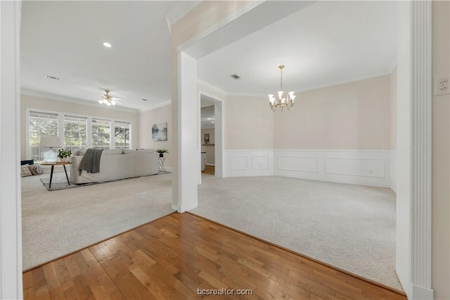 interior space featuring crown molding, visible vents, carpet flooring, wood finished floors, and ceiling fan with notable chandelier