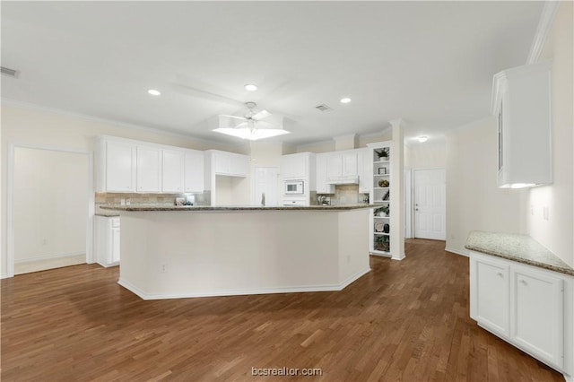 kitchen with tasteful backsplash, white microwave, dark wood-style flooring, white cabinetry, and open shelves