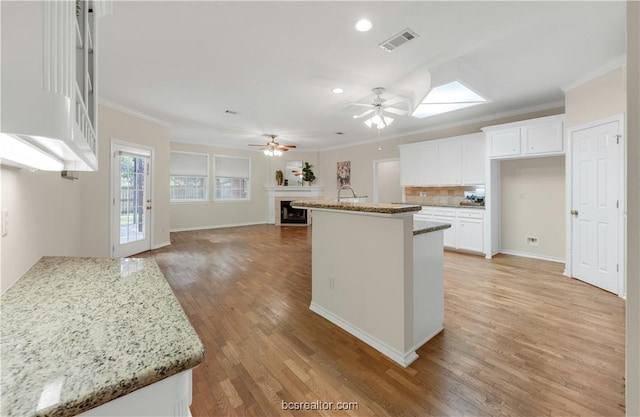 kitchen with crown molding, a fireplace, light wood finished floors, visible vents, and backsplash