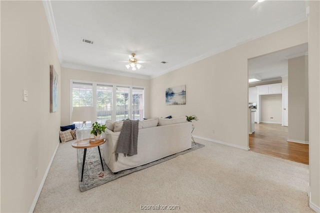 living area with baseboards, visible vents, light colored carpet, ceiling fan, and crown molding