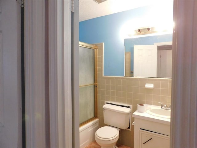 full bathroom with a textured ceiling, vanity, tile walls, enclosed tub / shower combo, and toilet