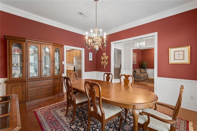 dining room with crown molding, visible vents, wainscoting, and a notable chandelier