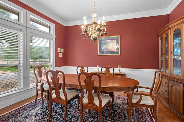 dining room with wood finished floors, ornamental molding, a wainscoted wall, and a notable chandelier
