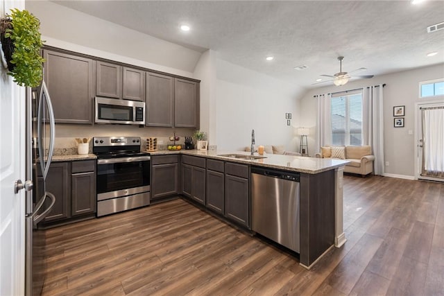 kitchen featuring light stone counters, stainless steel appliances, a peninsula, a sink, and open floor plan