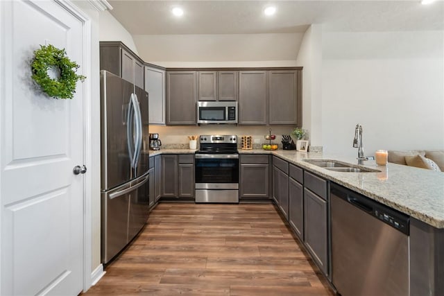 kitchen with a peninsula, dark wood-type flooring, a sink, appliances with stainless steel finishes, and light stone countertops