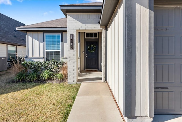 property entrance with board and batten siding, brick siding, a yard, and a shingled roof