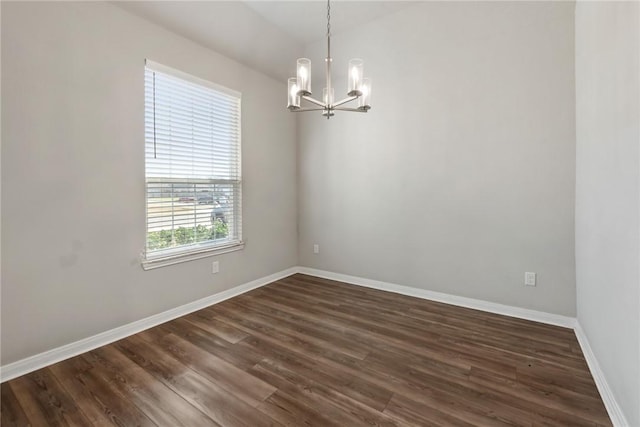 spare room with a chandelier, dark wood-type flooring, and baseboards