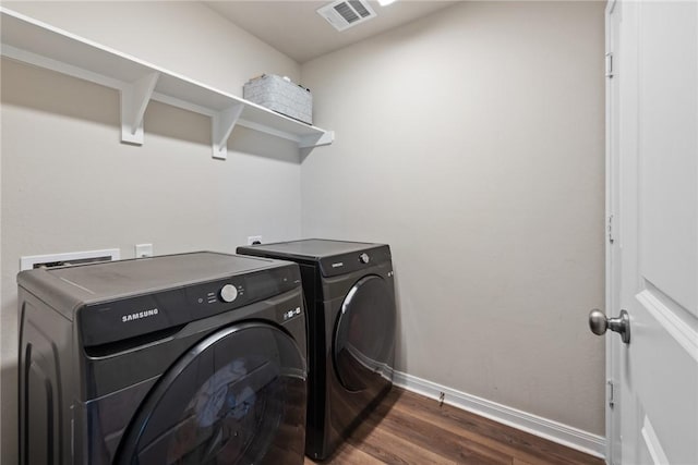 clothes washing area with dark wood finished floors, washer and clothes dryer, visible vents, laundry area, and baseboards