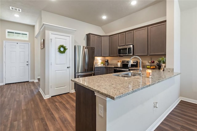 kitchen with appliances with stainless steel finishes, a sink, dark brown cabinets, light stone countertops, and a peninsula