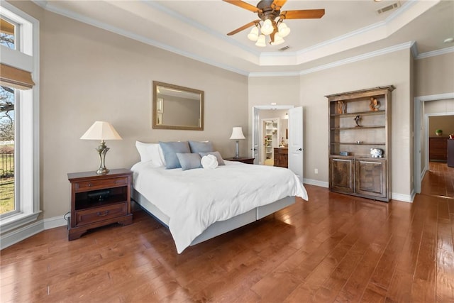bedroom with baseboards, visible vents, wood finished floors, ornamental molding, and a raised ceiling