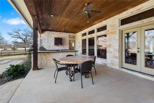 view of patio featuring french doors, fence, a ceiling fan, an outdoor kitchen, and outdoor dining area