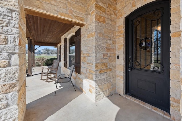 doorway to property featuring a porch and stone siding