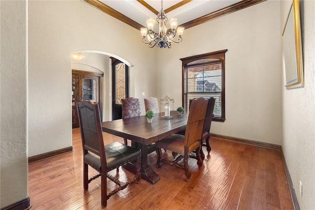 dining room with arched walkways, a notable chandelier, ornamental molding, and hardwood / wood-style flooring