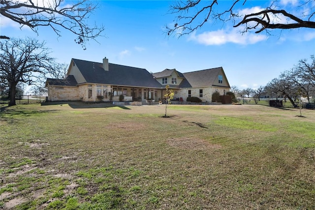 rear view of house featuring a lawn, stone siding, and a chimney