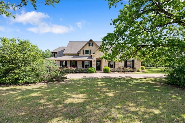 view of front of property with a front lawn, roof with shingles, and stone siding