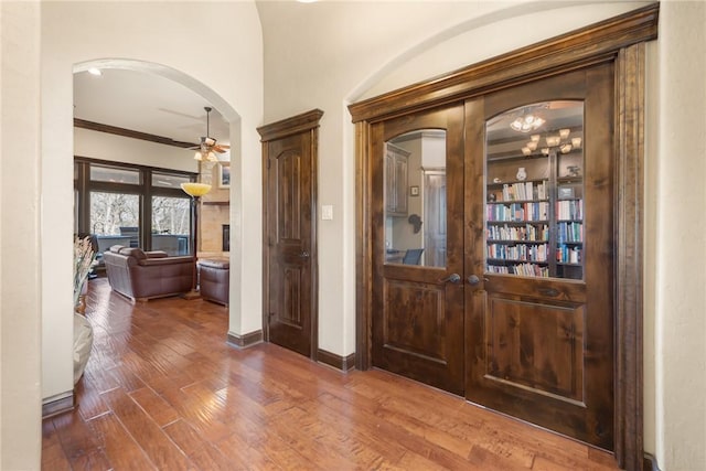 foyer entrance featuring wood finished floors, a ceiling fan, ornamental molding, arched walkways, and baseboards