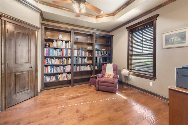 sitting room featuring baseboards, ornamental molding, ceiling fan, a tray ceiling, and wood finished floors