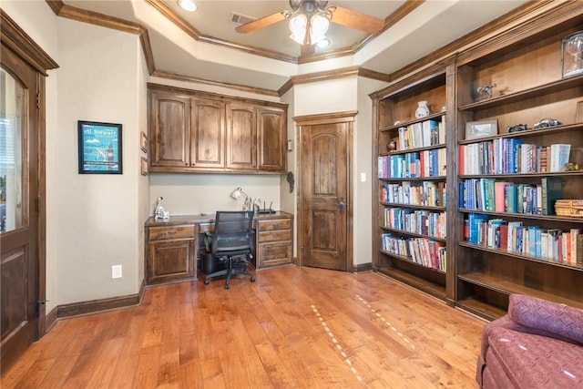 home office featuring built in desk, a ceiling fan, crown molding, a tray ceiling, and light wood finished floors