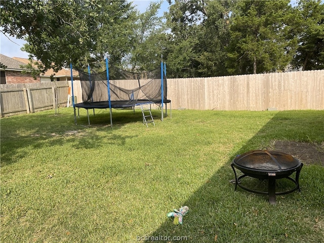 view of yard featuring a trampoline and an outdoor fire pit