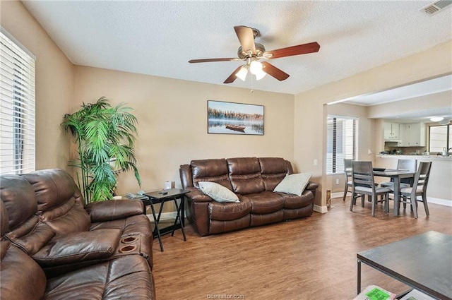 living area with visible vents, a textured ceiling, light wood finished floors, baseboards, and ceiling fan