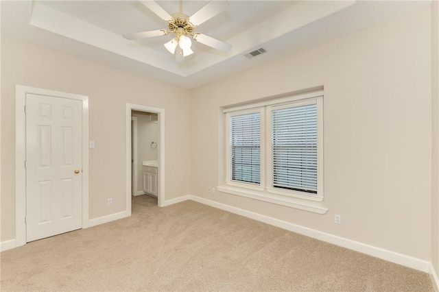 9300 Lakeside Ct, College Station, TX 77845 - unfurnished bedroom with light colored carpet, a tray ceiling, baseboards, ensuite bath, and a ceiling fan