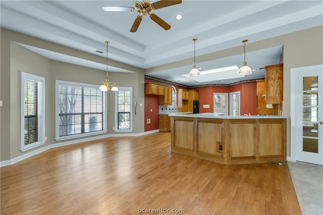 kitchen featuring hanging light fixtures, a raised ceiling, kitchen peninsula, ceiling fan with notable chandelier, and light wood-type flooring