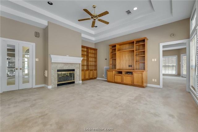 unfurnished living room with a fireplace, french doors, light carpet, and a tray ceiling