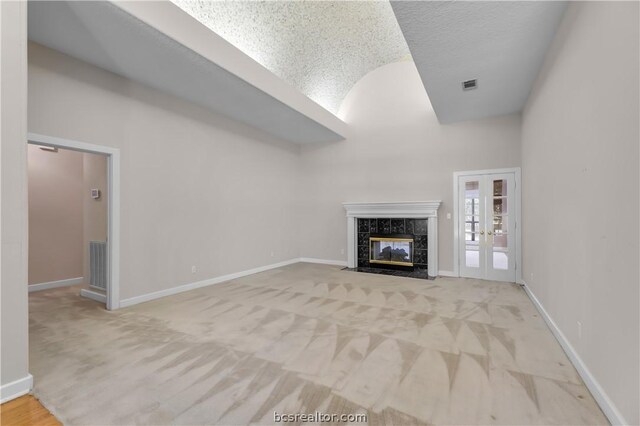 unfurnished living room featuring light carpet, french doors, a textured ceiling, and a premium fireplace