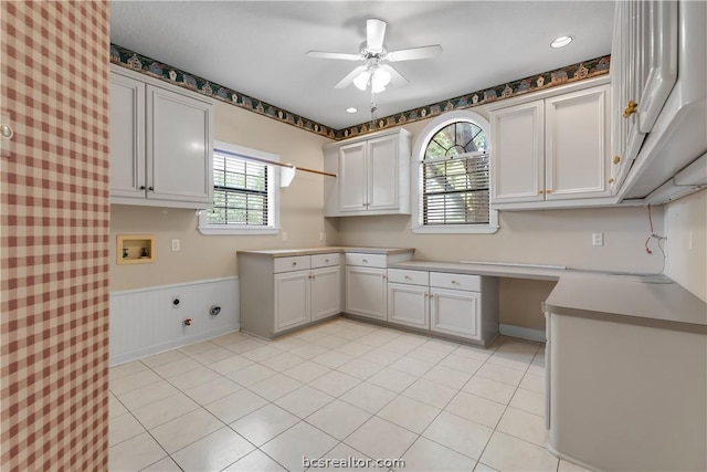 kitchen with white cabinets, ceiling fan, built in desk, and light tile patterned floors