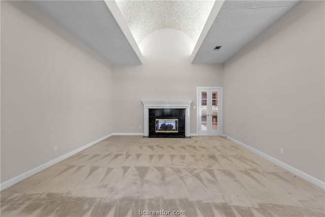 unfurnished living room featuring a tile fireplace, lofted ceiling, light colored carpet, and a textured ceiling