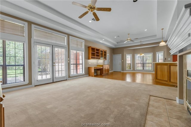 unfurnished living room featuring a tray ceiling, ceiling fan, and light colored carpet