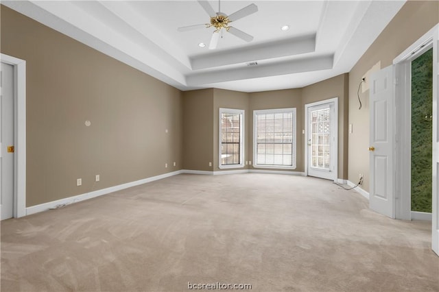 spare room with a raised ceiling, light carpet, and ceiling fan