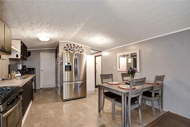 kitchen with lofted ceiling, ornamental molding, a sink, appliances with stainless steel finishes, and light wood-type flooring