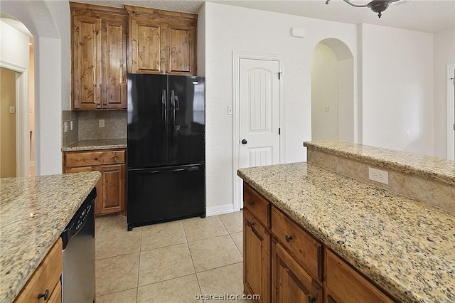 kitchen with light stone countertops, black fridge, stainless steel dishwasher, decorative backsplash, and light tile patterned floors