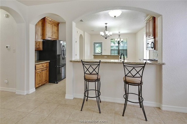 kitchen with a notable chandelier, black fridge, a kitchen bar, and light stone counters