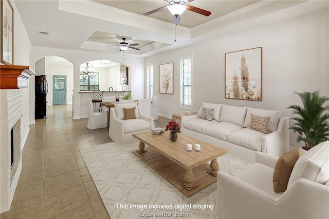 living room with a brick fireplace, a raised ceiling, ceiling fan, and light tile patterned flooring