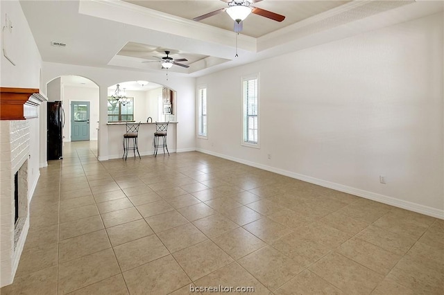 unfurnished living room with a tray ceiling, ceiling fan, light tile patterned floors, and a brick fireplace