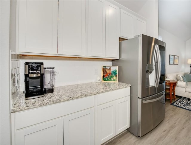 kitchen with stainless steel fridge, light stone countertops, white cabinets, and light wood-type flooring