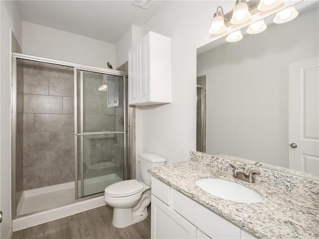 bathroom featuring wood-type flooring, a shower with shower door, vanity, and toilet