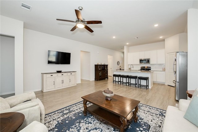 living room featuring ceiling fan, sink, and light wood-type flooring