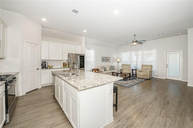 kitchen featuring sink, white cabinetry, light hardwood / wood-style floors, an island with sink, and black range with gas stovetop