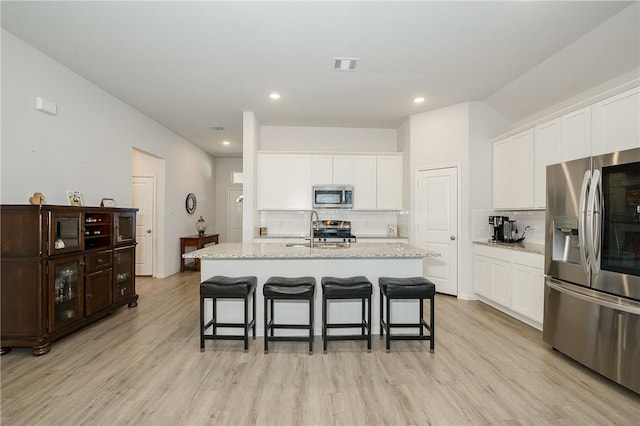 kitchen featuring white cabinetry, appliances with stainless steel finishes, a center island with sink, and light stone counters