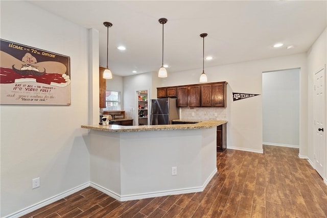 kitchen with kitchen peninsula, pendant lighting, stainless steel refrigerator, and dark wood-type flooring