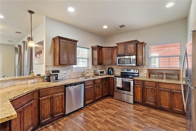 kitchen featuring pendant lighting, sink, dark hardwood / wood-style floors, kitchen peninsula, and stainless steel appliances