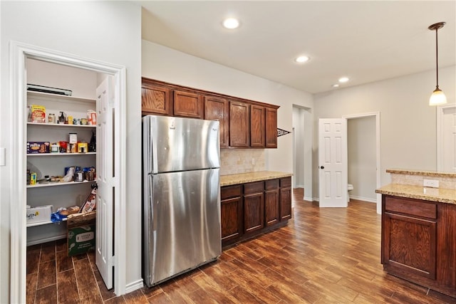 kitchen featuring dark wood-type flooring, hanging light fixtures, tasteful backsplash, light stone counters, and stainless steel fridge