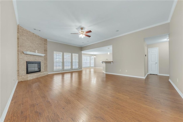 unfurnished living room with crown molding, wood-type flooring, ceiling fan with notable chandelier, and a brick fireplace