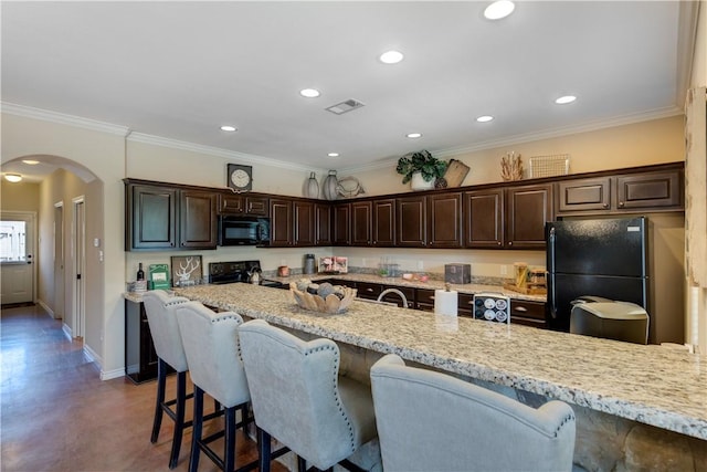 kitchen featuring dark brown cabinetry, a kitchen bar, visible vents, arched walkways, and black appliances