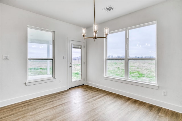 empty room featuring baseboards, visible vents, a chandelier, and wood finished floors